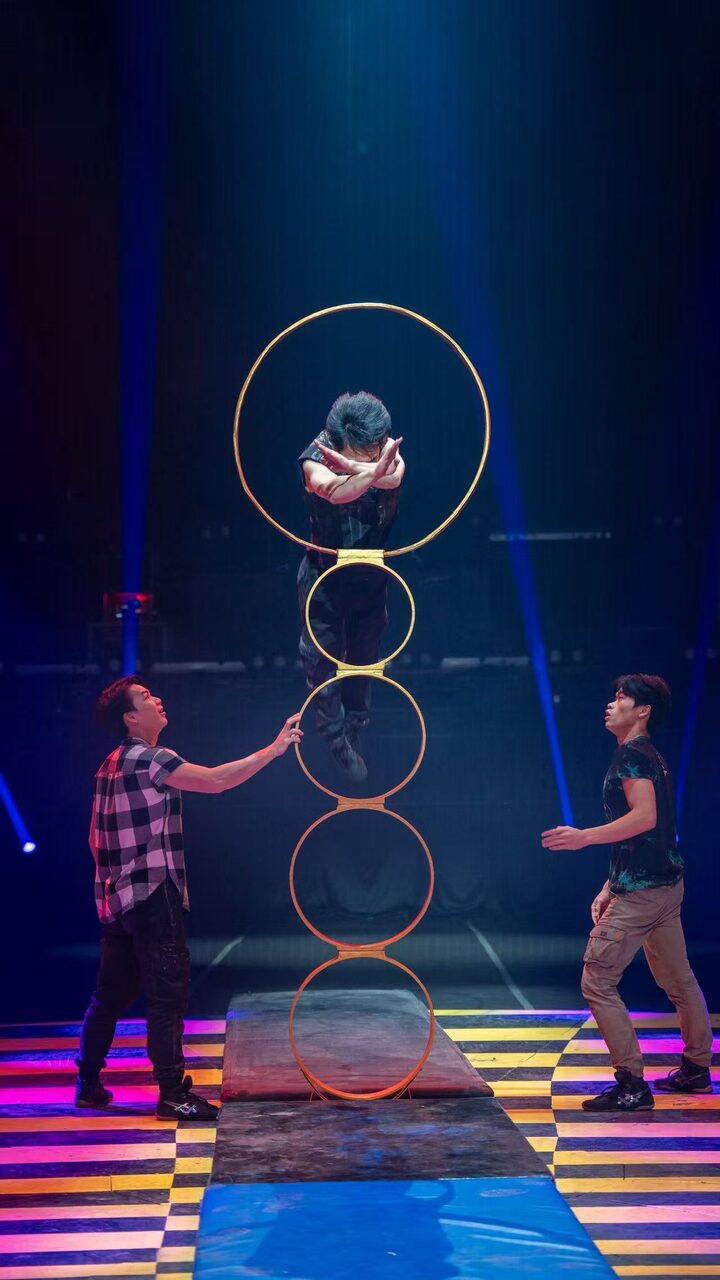 An acrobat diving head first through a stack of five hoops