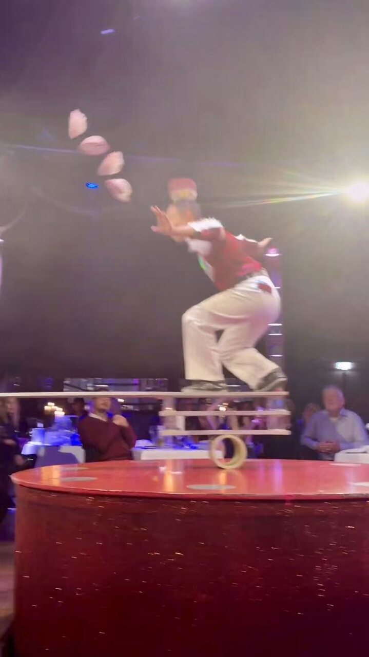 A juggler in a Santa costume balancing on a rolling board above the audience
